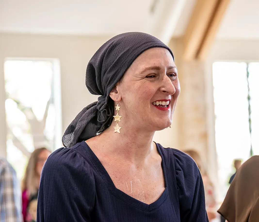 A breast cancer survivor smiles. She is wearing a black head scarf.