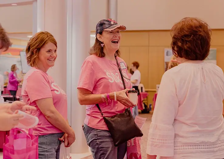 Two women wearing pink talk with another woman at an expo