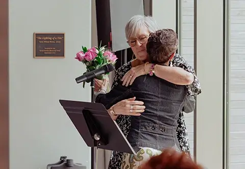 A woman hugs another woman and gives her a bouquet of flowers