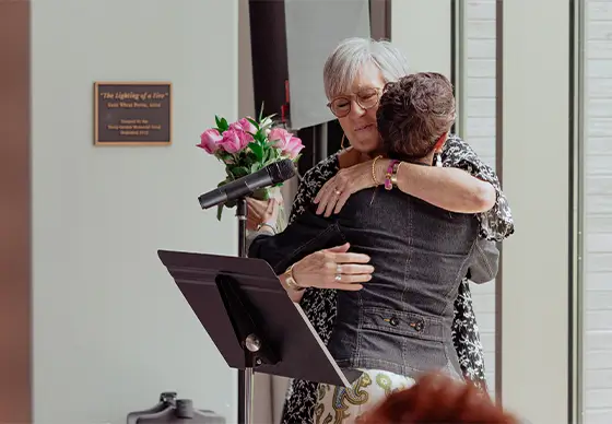 Two women embracing while holding flowers<br />
