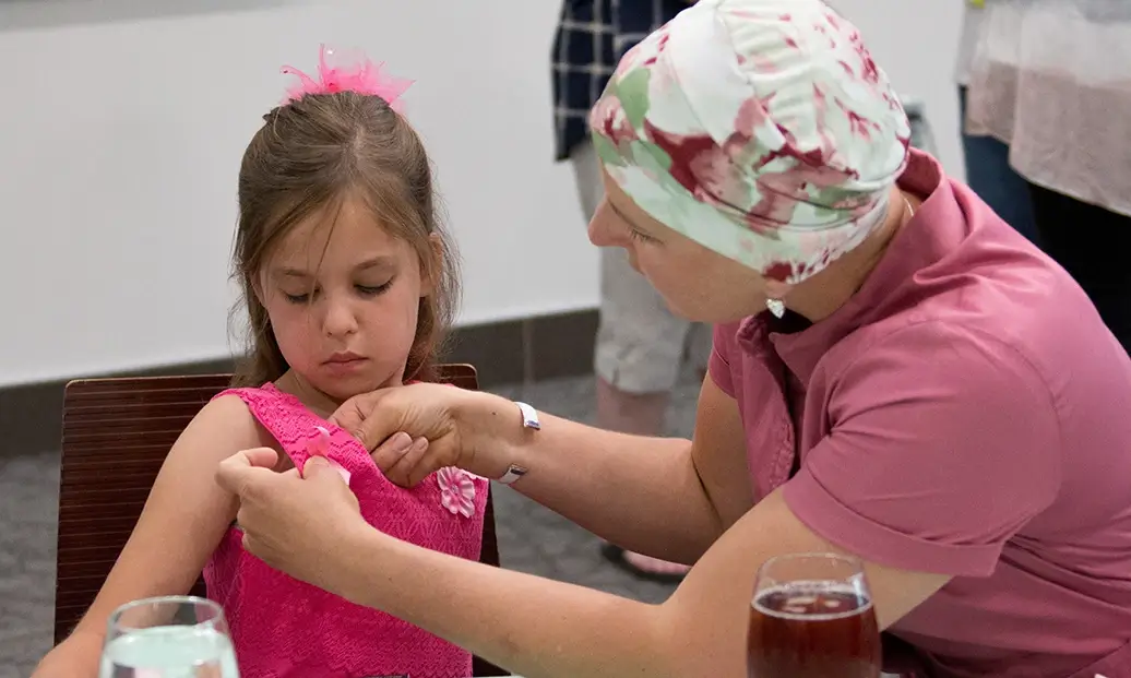 A woman with breast cancer pins a button on a little girl's pink dress