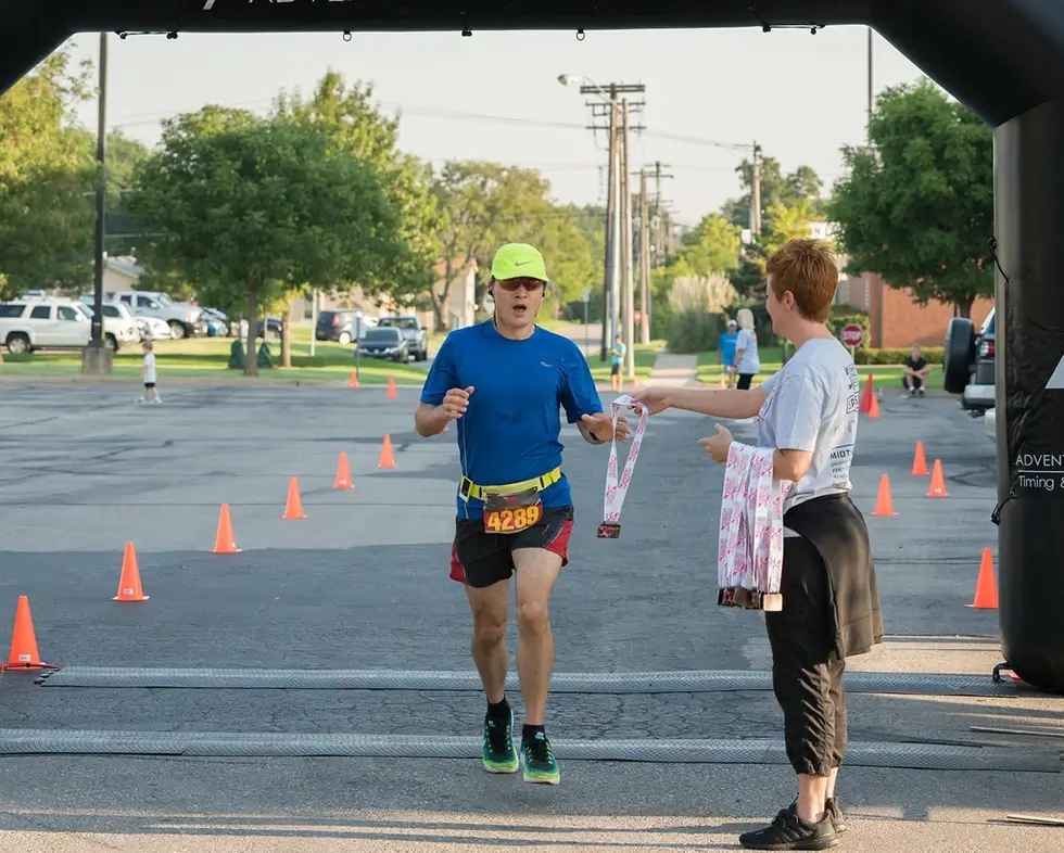 A man stops running at the finish line and is handed his medal. 