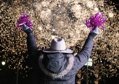 A woman raises pink pompoms while watching fireworks