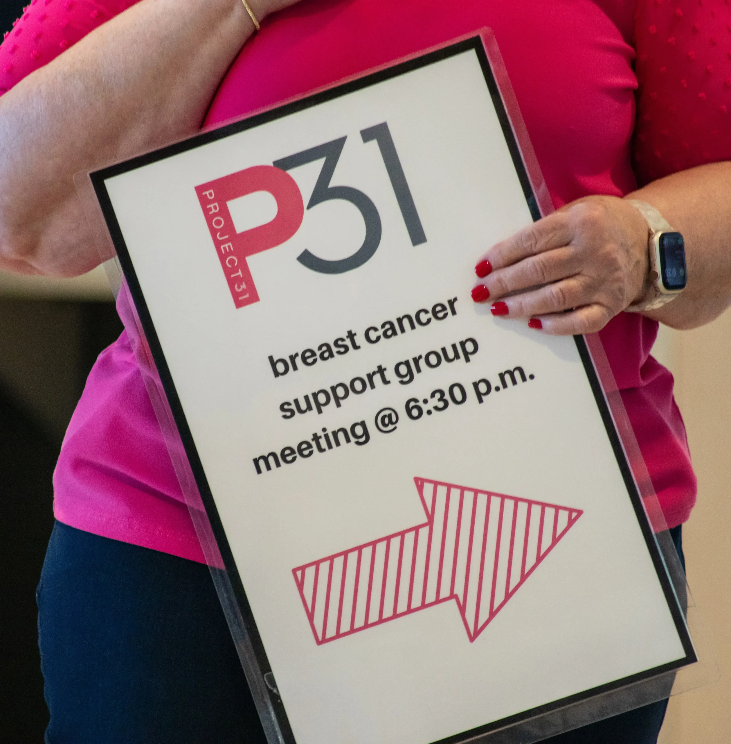 A woman holding a sign that says: breast cancer support group meeting @ 6:30 p.m.