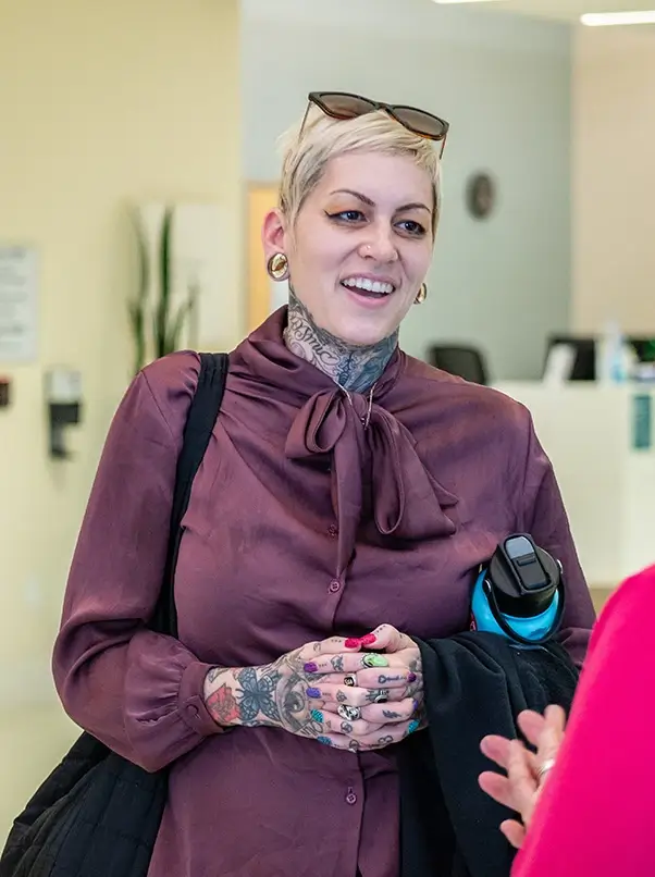 A woman with hand tattoos smiles and talks to another woman
