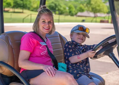 A mom smiles while her son holds a golf cart steering wheel